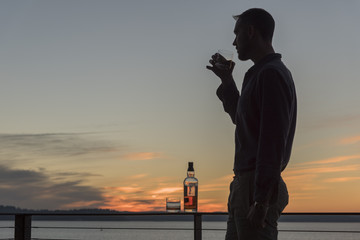 Silhouetted man at sunset drinking whiskey