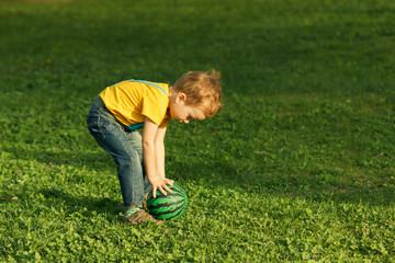 Fototapeta na wymiar Cute positive kid, playing happily with ball on green meadow