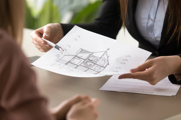 Close up view of female broker holding architectural house plan, signing lease agreement, meeting...