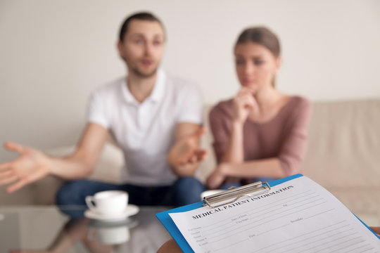 Unhappy man telling family psychologist his opinion about problems in marriage while his unsatisfied wife sitting next to husband during therapy session. Couple consulting relationships expert