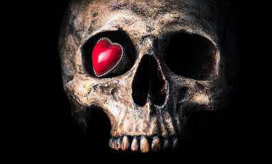 Obraz premium old heart shape ring in eye socket of human skull on black background