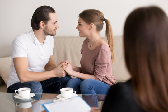 Excited loving couple sitting on sofa holding hands looking in the eyes, meeting with wedding planner, choosing place for honeymoon trip, successful marriage therapy with family psychologist