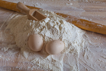 Bakery background. Flour, domestic eggs, wooden spoon for flour and a wooden rolling pin