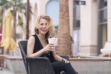 Young happy blond female having fun at open air terrace with a cup of coffee. Big city life. Happiness concept. Coffee drinking