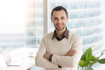 Smiling happy young businessman standing in office with arms crossed. Business owner, prospective promising manager, successful career in big corporation, company director looking at camera headshot