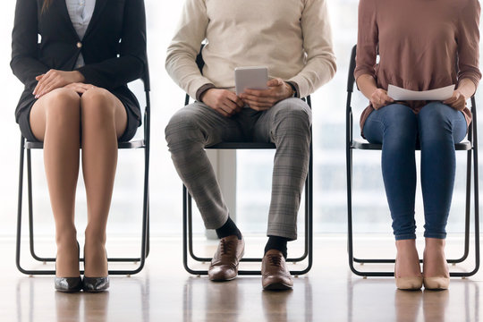 Three candidates for position waiting for their turn in job interview sitting on chairs, preparing for meeting, having audition, people in queue, human legs close up, job search concept