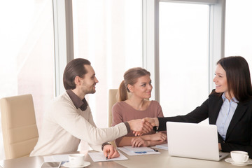 Young friendly businesswoman shaking hands with business partners during meeting sitting at office desk. Executive and employees handshaking starting briefing, work results report, nice to meet you