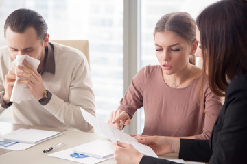 Young businessman with handkerchief caught flu sitting among colleagues on meeting discussing work...