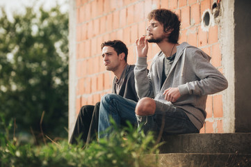 Depressed and sad young man smoking cannabis joint with friend