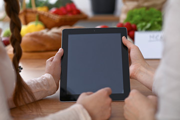 Human hands of two female persons using touchpad in the kitchen. Closeup of two women are making online shopping by tablet computer and credit card. Cooking and shopping concept