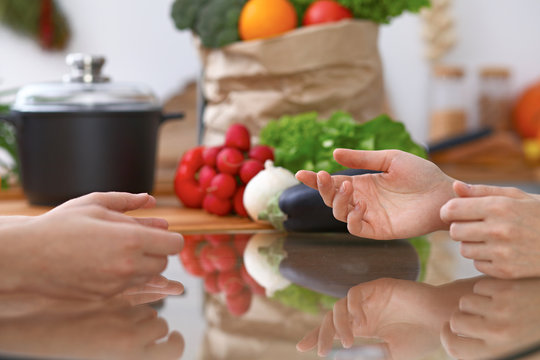 Two women discussing a new menu in the kitchen, close up. Human hands of two persons gesticulating at the table among fresh vegetables. Cooking and friendship concept