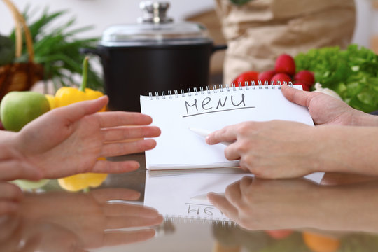 Human hands pointing into note book with copy space area. Two woman making menu in the kitchen, closeup. Cooking and friendship concept