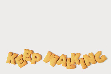 The word KEEP WALKING made with alphabet shaped biscuits isolated on white background