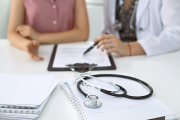 Stethoscope, medical prescription form are lying against the background of a doctor and patient discussing health exam results.