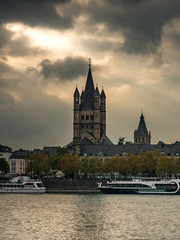 Great St. Martin Church Panoramic View and Tower Of City Hall across Rhine River Embankment, Old Town under Dramatic Sky Golden Summer Sunset Light Ray, Landmark in Cologne, Germany