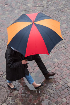 couple marchant avec un parapluie sur un place pavée