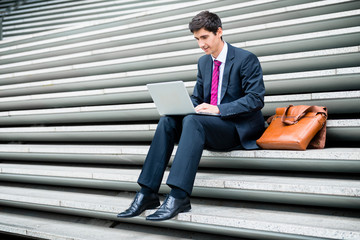 Young businessman using a laptop while sitting down outdoors