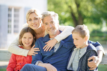 Portrait of happy family of four sitting on bench