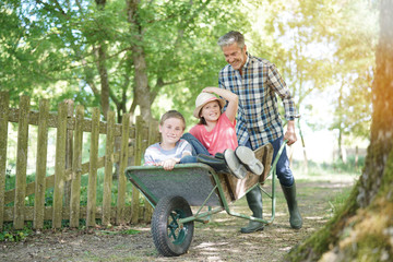 Daddy riding kids in wheelbarrow - obrazy, fototapety, plakaty