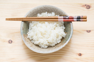 japanese rice in ceramic bowl with chopsticks on pine wood table