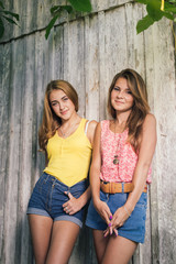 Fototapeta premium Two happy teenage girls friends wearing Tshirts and jeans shorts smiling over pale wooden background