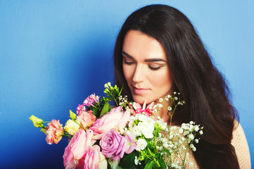 Close up portrait of 35-40 year old woman with black hair, holding big bouquet of spring flowers, standing against blue background