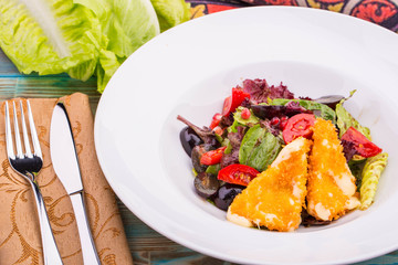 Fried suluguni cheese in breadcrumbs, is served from a mix of lettuce leaves with tomatoes and grapes