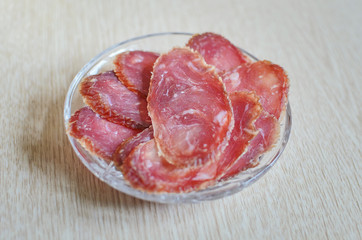 Sliced sausage from smoked chopped meat lies in a glass plate on the table.. Close-up, selective focus.