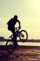Silhouette Cyclist, young man, at sunset near river, in a jump, vintage style.
