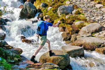 Female hiker crossing a mountain stream on stepping stones