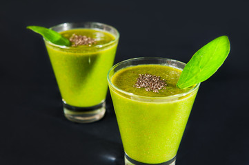 Close up Two glasses of healthy green smoothie with chia seeds and spinach leafes on the dark background isolated. Selective focus