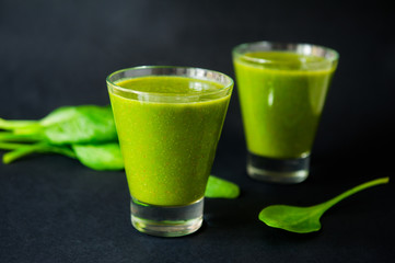 Two glasses of healthy green smoothie with spinach leafes on the dark background isolated. Selective focus