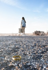 Chica recién divorciada de espaldas con maleta de viaje andando por la carretera.