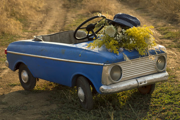 Childhood memory. Old child car toy with a bouquet of flowers and a straw hat in the middle of a...
