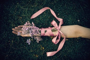 Female hand with bouquet of lilac flowers - Hand of a woman over the grass with ribbon bow and...