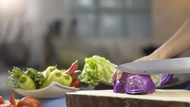 Slicing purple cabbage with kitchen knife on wooden board, close up, uhd 4k.

