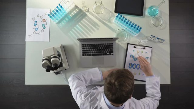 Medical student studying DNA image, making notes on laptop, genetics, top view