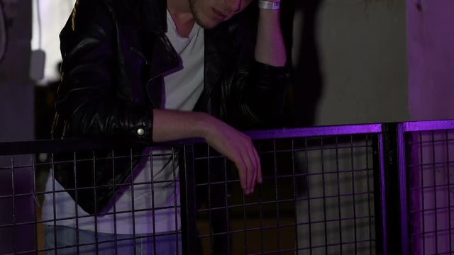 Upset young man suffering depression after breakup, standing alone at party