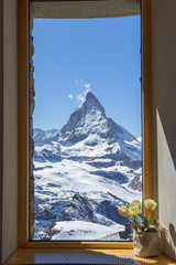 Scenic view on snowy Matterhorn peak in sunny day with blue sky and blur window in foreground, Switzerland.
