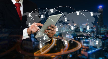 smart businessman in suit using his tablet, business and technology concept with world map social media network connection on blurred night city background, color tone effect, wide screen.