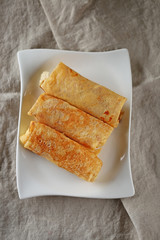 Three stuffed with cottage cheese pancake On a white rectangular plate on a beige linen tablecloth
