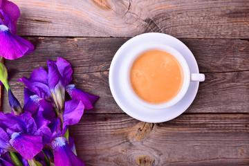 cup of coffee on a saucer next to a bouquet of purple irises