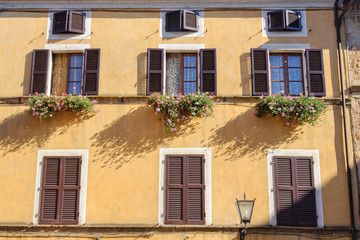 Fototapeta na wymiar Butter facade with windows, shutters, flower pots and street light - Pienza, Tuscany, Italy