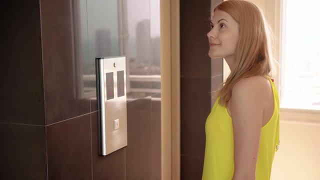 Beautiful young woman in yellow dress waiting for an elevator. Pushing a button calling up a lift