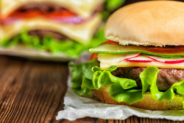 close up of fresh home made hamburgers with beef, cucumber, radish, lettuce, cheese and spices on wooden rustic table