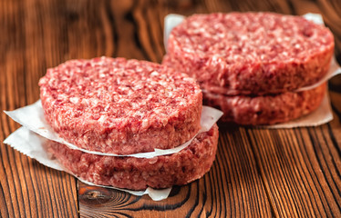 raw ground beef meat hamburger patties on paper, wooden background