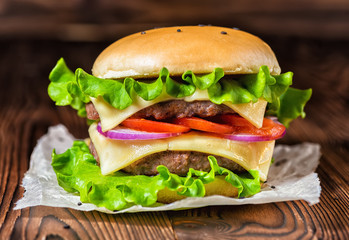homemade full cheeseburger with vegetables, spices and beef meat on dark wooden background