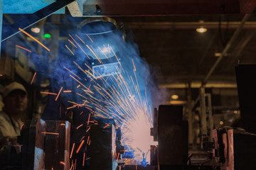 Industrial worker is welding metal part in factory
