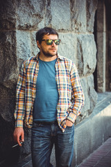 Obraz premium A man, a resident of a large metropolis, leads an unhealthy lifestyle, stands and smokes cigarettes near a local bar
