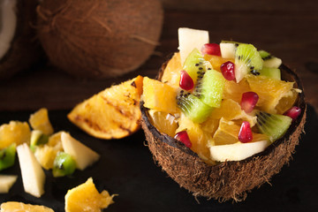 Juicy colorful fruits chopped in coconut shell on rustic wooden table, top view. Appetizing and tasty vegetarian dish, healthy food.